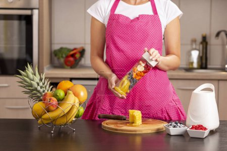 Téléchargez les photos : Détail des mains féminines fermant un bol de mélangeur rempli de fruits frais avant de faire un smoothie pour le petit déjeuner - en image libre de droit