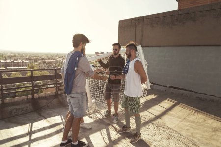Téléchargez les photos : Groupe de jeunes amis se préparant à jouer footbal sur la construction terrasse sur le toit, choisir des équipes avant le match - en image libre de droit