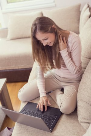 Foto de Joven hermosa mujer sentada en un sofá en la sala de estar, disfrutando de su tiempo libre y utilizando una computadora portátil - Imagen libre de derechos