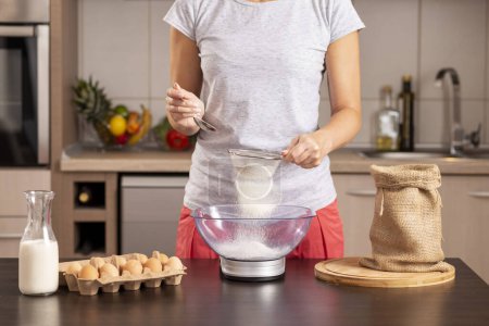 Foto de Detalle de las manos femeninas usando una escala de cocina para medir la harina; mujer midiendo los ingredientes para hacer un pastel, tamizando la harina - Imagen libre de derechos