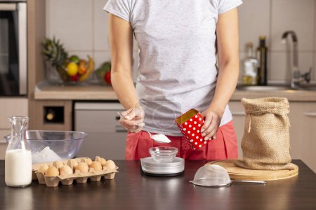 Foto de Detalle de manos femeninas usando una balanza de cocina para medir azúcar; mujer midiendo ingredientes para hacer un pastel. Concéntrate en la cuchara y la mano - Imagen libre de derechos