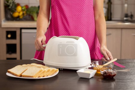 Foto de Detalle de manos femeninas encendiendo una tostadora, haciendo pan tostado para el desayuno. Enfócate en el interruptor de tostadora en el mango - Imagen libre de derechos