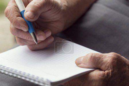 Téléchargez les photos : Détail des mains d'une femme âgée tenant un stylo et écrivant une liste d'épicerie. Concentration sélective - en image libre de droit