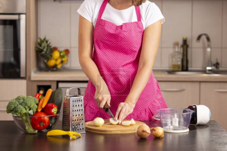 Foto de Detalle de las manos femeninas cortando cebollas peladas con un cuchillo de cocina en una tabla de cortar - Imagen libre de derechos