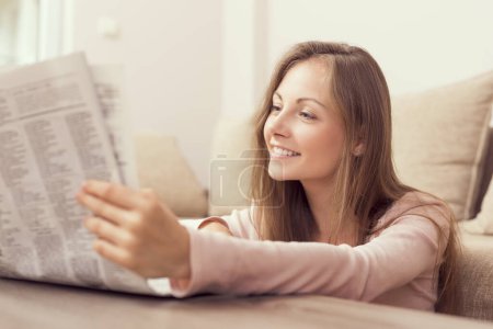 Foto de Mujer joven sentada en el piso de la sala de estar junto a una mesa de café y leyendo los periódicos - Imagen libre de derechos