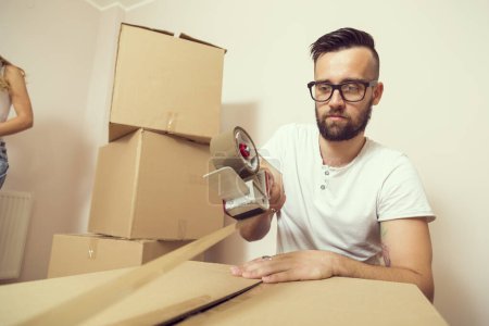 Photo for Young man packing things and taping boxes, preparing for moving out the appartment - Royalty Free Image