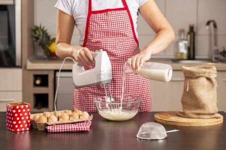 Foto de Detalle de la mano femenina sosteniendo la batidora, vertiendo la leche en un tazón y mezclando una masa de panqueque - Imagen libre de derechos