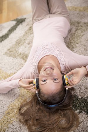 Téléchargez les photos : Vue de dessus d'une belle brune allongée sur le tapis sur le sol de son appartement, écoutant la musique et profitant de son temps libre - en image libre de droit