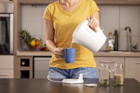 Foto de Mujer haciendo una taza de té por la mañana, vertiendo un agua hirviendo de una tetera en una taza - Imagen libre de derechos