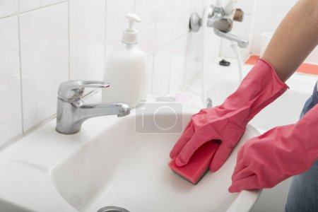 Téléchargez les photos : Gros plan des mains féminines portant des gants de protection, lavabo de salle de bain avec éponge - en image libre de droit