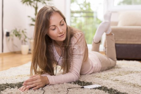 Foto de Hermosa morena tumbada en la alfombra en el suelo de su apartamento, escuchando la música y disfrutando de su tiempo libre - Imagen libre de derechos