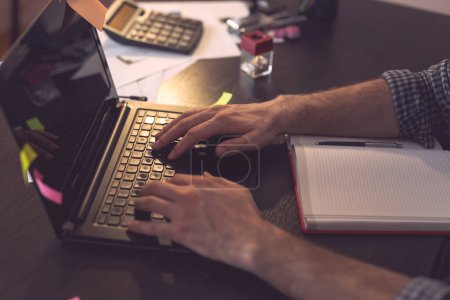 Téléchargez les photos : Détail des mains masculines tapant sur le clavier d'un ordinateur portable ; pigiste travaillant dans un bureau à domicile. Focus sélectif sur le clavier et les doigts - en image libre de droit
