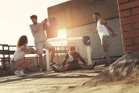 Téléchargez les photos : Groupe de jeunes amis s'étirant avant de jouer un match de football sur un toit de bâtiment - en image libre de droit