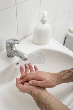 Téléchargez les photos : Gros plan d'un homme se lavant les mains sur le lavabo de la salle de bain. Focus sélectif sur la main - en image libre de droit