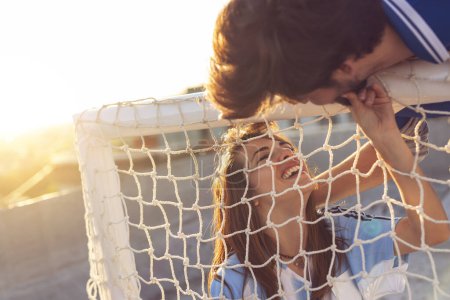 Téléchargez les photos : Couple amoureux portant des maillots de football sur le toit d'un immeuble après un match, profitant d'un magnifique coucher de soleil sur la ville - en image libre de droit