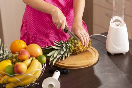 Photo for Woman cutting a pineapple top with a kitchen knife on a cutting board in order to peel it with a pineapple cutter - Royalty Free Image