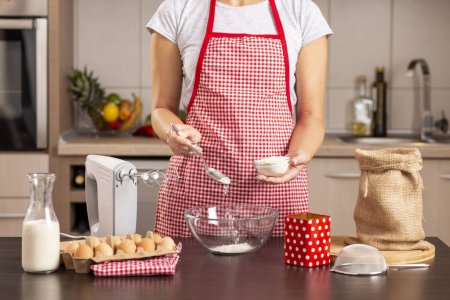 Foto de Detalle de las manos femeninas añadiendo harina en un tazón para mezclar mientras se hace un pastel - Imagen libre de derechos