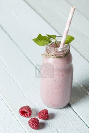 Photo for Raspberry smoothie in a bottle, decorated with drinking straw and mint leaves with raspberry fruit set next to it on the wooden board background. Selective focus - Royalty Free Image