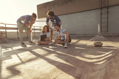 Foto de Grupo de jóvenes amigos divirtiéndose jugando un partido de fútbol en una terraza de la azotea del edificio, tomando un tiempo fuera, planeando la estrategia del juego y dibujándolo en el tablero - Imagen libre de derechos