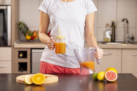 Photo for Detail of female hands holding a jug of freshly squeezed mixed citrus fruit and pouring it into a jar - Royalty Free Image