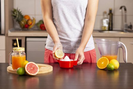 Téléchargez les photos : Détail des mains féminines tenant la moitié du citron et le pressant avec un presse-citron ; femme faisant de la limonade sur un comptoir de cuisine. Focus sur le presse-citron - en image libre de droit
