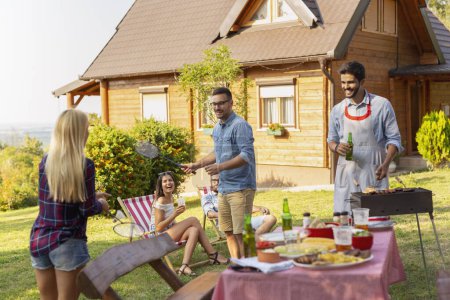 Photo for Group of friends having a backyard barbecue party, grilling meat, drinking beer, playing badminton and having fun on a sunny summer day. Focus on the man playing badminton - Royalty Free Image