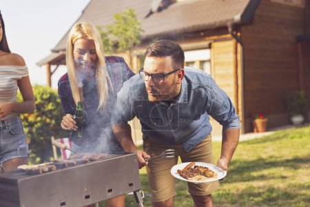 Téléchargez les photos : Groupe d'amis faisant barbecue dans la cour arrière et s'amusant par une journée d'été ensoleillée - en image libre de droit