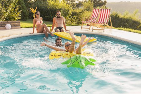Photo for Couple in love at a poolside summer party, sunbathing and having fun; girl floating in the pool on a pineapple shaped air mattress - Royalty Free Image