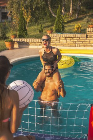 Téléchargez les photos : Groupe d'amis s'amuser à une fête au bord de la piscine en été, jouer au volley-ball dans la piscine - en image libre de droit