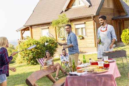 Photo for Group of friends having a backyard barbecue party, grilling meat, drinking beer, playing badminton and having fun on a sunny summer day - Royalty Free Image