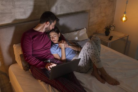 Téléchargez les photos : Homme travaillant tard dans la nuit, assis dans son lit et utilisant un ordinateur portable pendant que sa femme dort à côté de son - en image libre de droit