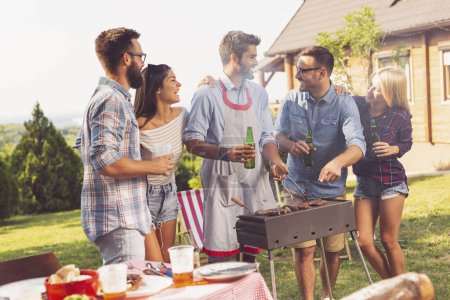 Téléchargez les photos : Groupe d'amis faisant un barbecue dans la cour, buvant de la bière et s'amusant par une journée d'été ensoleillée - en image libre de droit