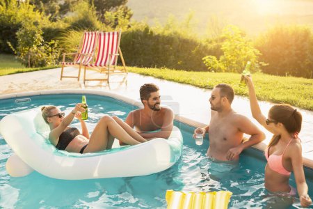 Photo for Group of friends at a poolside summer party, drinking cocktails and beer and having fun in the swimming pool - Royalty Free Image