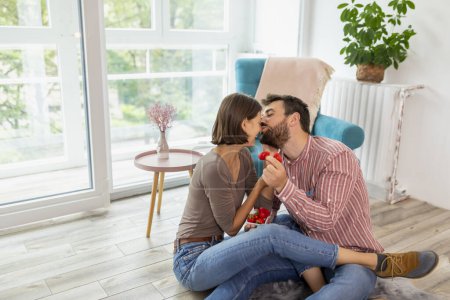 Téléchargez les photos : Couple amoureux assis sur le sol dans leur nouvelle maison, manger des fraises, rire et s'amuser - en image libre de droit