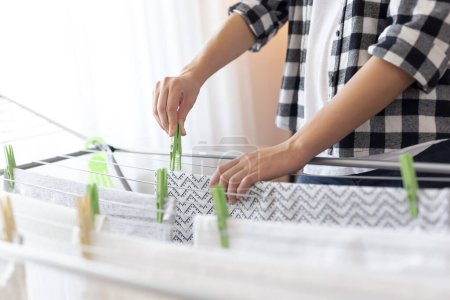 Photo for Detail of female hands hanging the washing out to dry on a drying rack. Focus on the clothespin and the hand holding it - Royalty Free Image