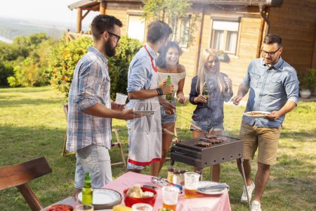 Photo for Group of friends making barbecue in the backyard, drinking beer and having fun on a sunny summer day. Focus on the man on the right - Royalty Free Image