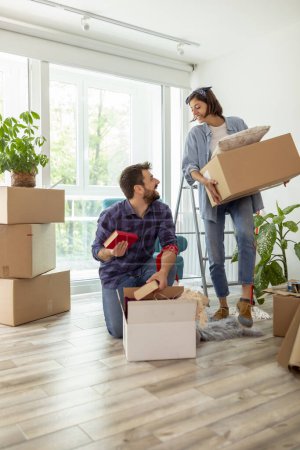 Photo for Beautiful young couple in love having fun unpacking things from cardboard boxes while moving in together in their new apartment - Royalty Free Image