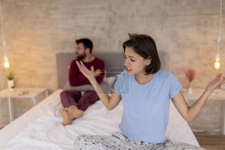 Photo for Young couple having an argument in bed, yelling at each other, displeased and angry - Royalty Free Image