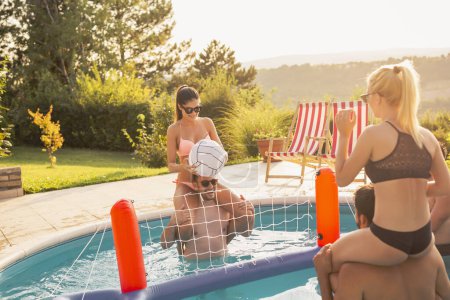 Téléchargez les photos : Groupe d'amis s'amuser à une fête au bord de la piscine en été, jouer au volley-ball dans la piscine - en image libre de droit