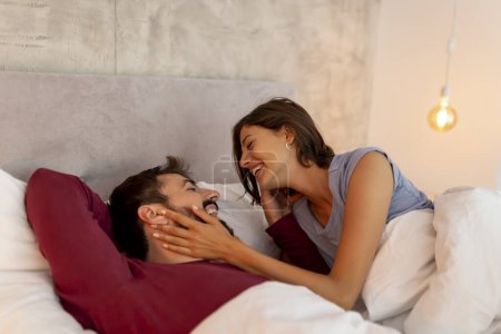 Téléchargez les photos : Beau jeune couple amoureux couché au lit après s'être réveillé le matin, riant, s'embrassant et appréciant le temps ensemble - en image libre de droit