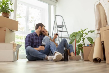Téléchargez les photos : Beau jeune couple amoureux célébrant déménagement dans une nouvelle maison, boire du vin, rire et s'amuser - en image libre de droit
