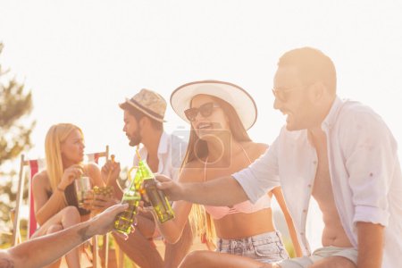 Téléchargez les photos : Groupe d'amis à une fête d'été au bord de la piscine, assis au bord d'une piscine, boire des cocktails et de la bière et s'amuser - en image libre de droit