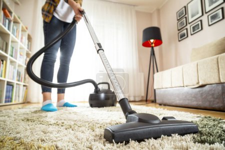Photo for Detail of a young woman doing home chores, vacuuming the living room carpet - Royalty Free Image
