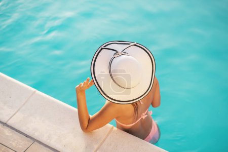 Téléchargez les photos : Jolie jeune femme portant un bikini et un chapeau, debout dans la piscine, bronzant et relaxant - en image libre de droit