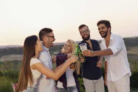 Téléchargez les photos : Groupe d'amis à une fête en plein air estivale s'amuser, danser, boire de la bière et porter un toast - en image libre de droit