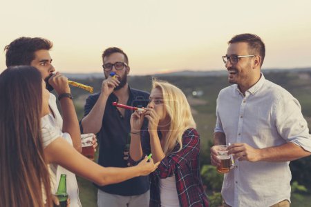 Téléchargez les photos : Groupe d'amis à une fête en plein air estivale s'amuser à siffler, danser et boire de la bière - en image libre de droit