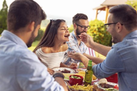 Téléchargez les photos : Groupe d'amis ayant un déjeuner barbecue extérieur, manger de la viande grillée, boire de la bière et s'amuser - en image libre de droit