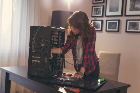 Photo for Young woman using electrical screwdriver for fixing a computer - Royalty Free Image