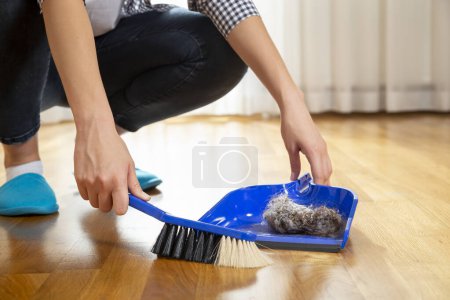 Foto de Detalle de las manos femeninas sosteniendo una escoba y barriendo el suelo, recogiendo polvo en un basurero - Imagen libre de derechos