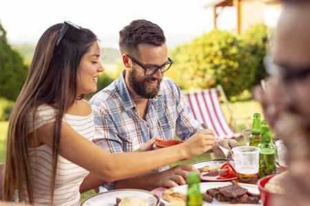 Téléchargez les photos : Groupe d'amis ayant un déjeuner barbecue extérieur, manger de la viande grillée, boire de la bière et s'amuser - en image libre de droit